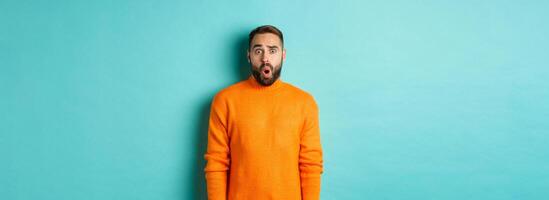 Shocked and confused man looking in awe at promo offer, standing near copy space on turquoise background photo