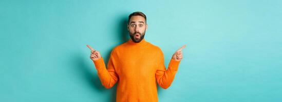 Shopping and advertisement concept. Excited man buyer pointing fingers sideways, showing two choices products, left and right banners, standing over light blue background photo