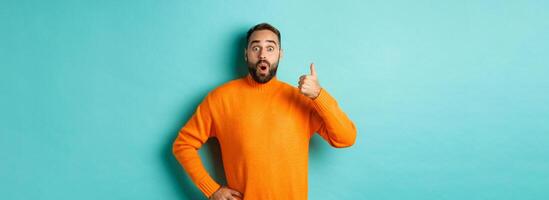 Well done. Handsome bearded man showing thumb up, praising good work, recommend excellent product, like and approve, smiling satisfied, standing over light blue background photo