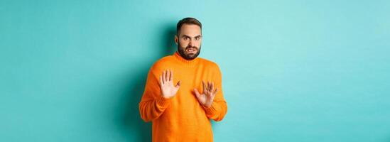 Alarmed guy shaking hands in rejection, declining and stepping away scared, standing over light blue background photo