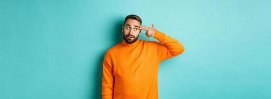 Man shooting himself in head, make finger gun near temple and roll eyes annoyed, standing bothered against light blue background photo