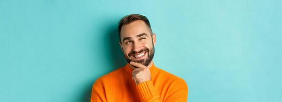 Close-up of caucasian male model having an idea, smiling and looking upper left corner thoughtful, imaging plan, standing over light blue background photo