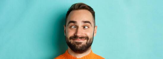 Headshot of funny caucasian man making faces, squinting and smiling silly, standing over light blue background photo