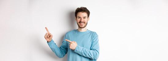 Happy bearded man showing advertisement, pointing fingers right and smiling, inviting to click link, standing over white background photo