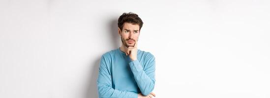 Young bearded man looking pensive and frowning, thinking about problem or trouble, standing worried against white background photo