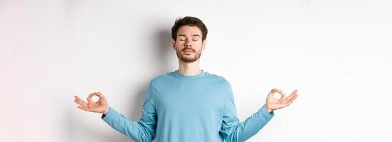 Young man trying to relax in meditation, standing calm with stretch out hands in zen mudra gesture, practice yoga on white background photo