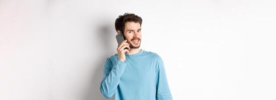Technology concept. Young male model talking on mobile phone, calling someone on smartphone and smiling, standing over white background photo