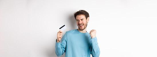 Happy man dancing with plastic credit card, smiling and saying yes, celebrating on white background photo