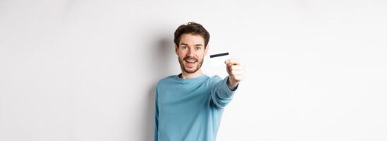 Happy man showing plastic credit card and smiling, recommending bank, standing over white background photo