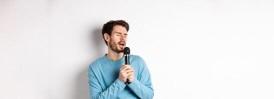 Young caucasian man singing song in microphone with carefree face, standing in karaoke over white background photo