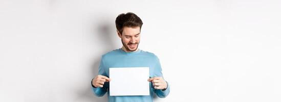 Young caucasian man looking at empty paper, reading logo, standing on white background photo