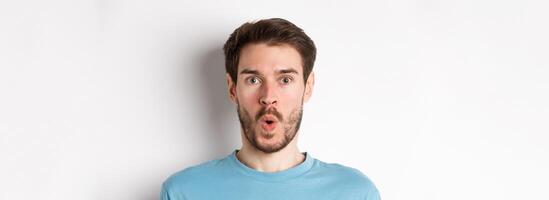 Close-up of surprised man face, saying wow and staring at camera amazed, standing on white background photo