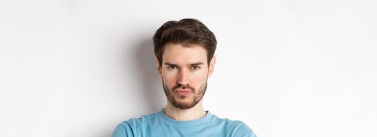 Close-up of grumpy young man grimacing, sulking and making offended face, standing upset over white background photo