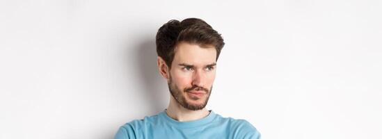 Close-up of disappointed bearded man, sulking and looking left with pensive face, standing upset over white background photo