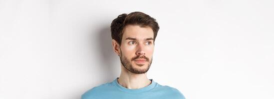 Close-up of handsome male model with beard and moustache, looking left with thoughtful face, standing over white background photo