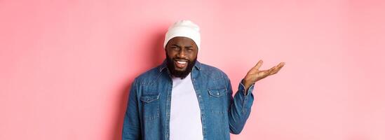 Annoyed and pissed-off african-american man pointing finger at head, scolding someone stupid, staring bothered at camera, pink background photo