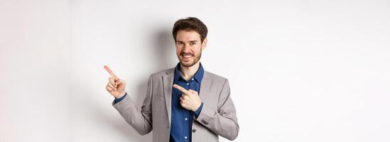 Handsome smiling man in business suit pointing fingers at upper right corner, showing logo, advertising company, standing on white background photo