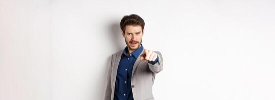 Confident and motivated businessman in suit need you, pointing finger at camera with encouraging face, choosing person, standing on white background photo