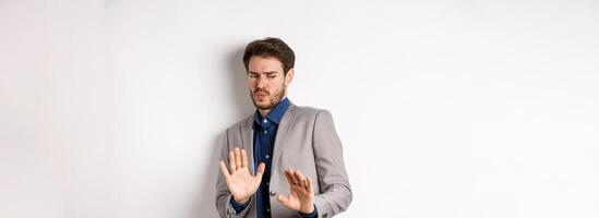 Stay away. Reluctant businessman step back with concerned disgusted face, raising hands to block bad offer, rejecting something awful, tilting from disgust, white background photo