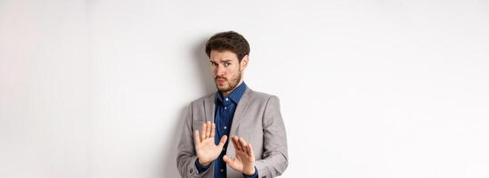 Stay away. Reluctant businessman step back with concerned disgusted face, raising hands to block bad offer, rejecting something awful, telling no and decline proposal, white background photo