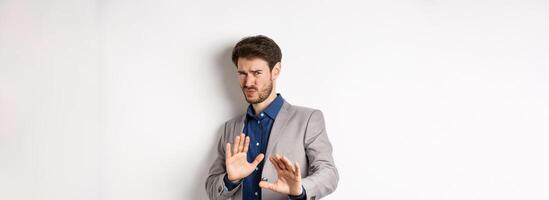 Stay away. Reluctant businessman step back with concerned disgusted face, raising hands to block bad offer, rejecting something awful, telling no and decline proposal, white background photo