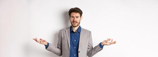 So what big deal. Confused and annoyed businessman spread hands sideways and frowning puzzled, cant understand whats wrong, standing on white background photo