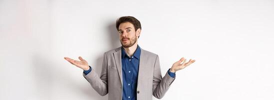 I dont know. Clueless bussiness man in suit shrugging shoulders and looking unaware, have no idea, standing on white background photo