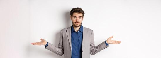 Dont know. Confused businessman spread hands sideways and look clueless, cant help, have no idea, standing on white background in suit photo