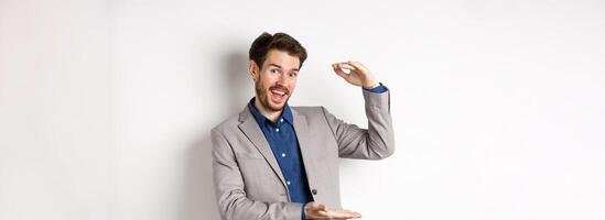 Handsome salesman in suit showing big size, large income, smiling at camera enthusiastic, standing on white background photo
