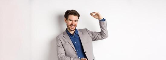 Successful businessman showing big size, shape large object and smiling pleased, standing on white background in suit photo