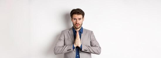 Sad cute business man need help, say please or sorry, showing begging gesture, asking for favour, standing on white background photo