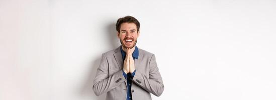 Happy caucasian businessman say thank you, smiling and laughing with hands showing namaste sign, express gratitude, standing on white background photo