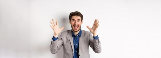Businessman scream and shake hands in panic, look alarmed and anxious, shouting at camera, standing in suit on white background photo