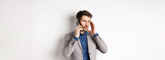 Businessman talking on phone and covering ear, receive call in loud place, cant hear caller, standing on white background photo