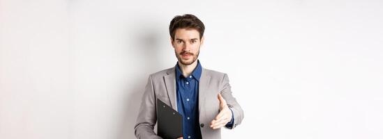 Confident businessman with clipboard giving hand for handshake, greeting business partners on meeting, standing on white background in suit photo
