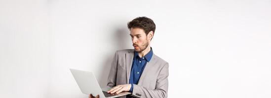 Excited salesman looking at laptop screen amazed, tilt away from excitement, checking out news in network, standing against white background photo