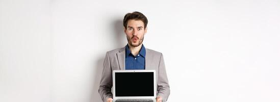 Handsome caucasian businessman in suit showing empty laptop screen, demonstrate promo, standing on white background photo