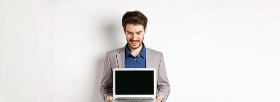 Handsome caucasian businessman in suit showing empty laptop screen, demonstrate promo, standing on white background photo
