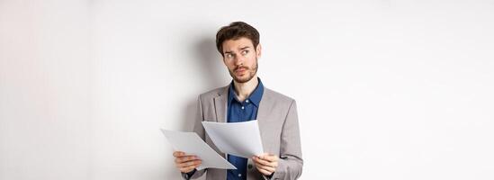 Businessman in suit looking through papers, reading documents at work and thinking, looking aside at logo, standing busy on white background photo