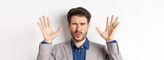 Close-up of disappointed and disgusted businessman raising hands up, grimacing from dislike and aversion, standing reluctant on white background photo