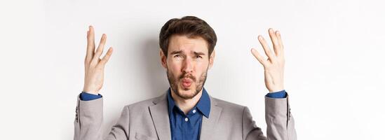 Frustrated businessman shaking hands and asking wtf what happened, looking disappointed and shocked at camera, scolding employee, white background photo