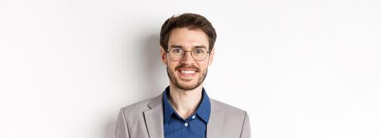 Close-up of handsome young office worker in glasses and suit smiling at camera, looking happy on white background photo