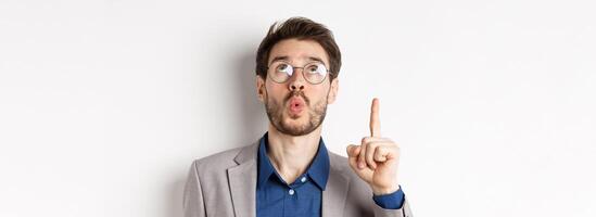 Excited handsome man in glasses and business suit, look up and pointing at top advertisement, exclaim wow with amazed expression, white background photo