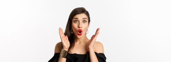 Fashion and beauty concept. Close-up of excited woman with makeup and red lipstick on, looking surprised and glad, standing over white background photo