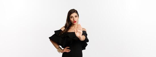 Fashion and beauty. Confident attractive woman telling no, showing stop gesture and looking serious at camera, disapprove and prohibit, standing over white background photo