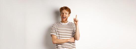 Young man with red hair having an idea, raising finger to say suggestion, standing happy over white background photo