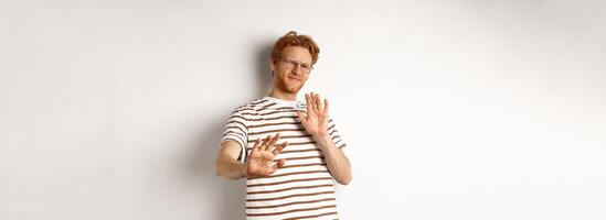 Displeased young man with red hair and bristle showing stop gesture, refusing something bad with disgusted face, standing over white background photo
