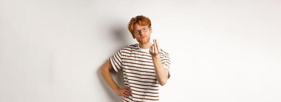 Image of satisfied young man with red hair and glasses showing chefs kiss gesture to praise something perfect, standing over white background photo