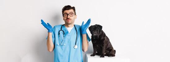Clueless doctor veteriantian in scrubs shrugging, staring at camera confused while dog sitting on examination table and waiting for check-up, white background photo