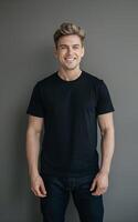 A portrait of a man in a black t-shirt and jeans, standing against a neutral grey background. photo